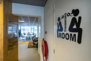 Ingang van een modern kantoor aan de De Ruijterkade met zicht op werkplekken en een deur met het opschrift "Thinking Room".